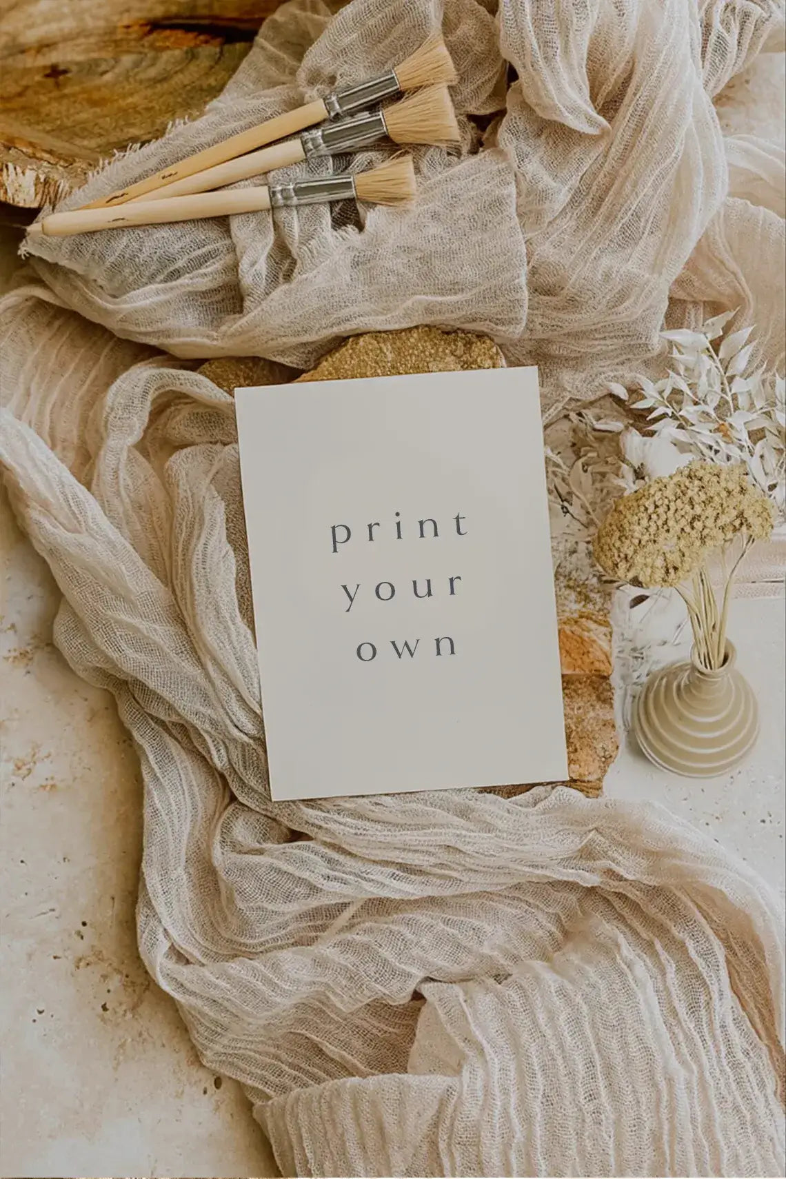 Minimalist ‘Print Your Own’ card placed on soft beige fabric with artist paintbrushes and dried florals in a neutral-toned setting